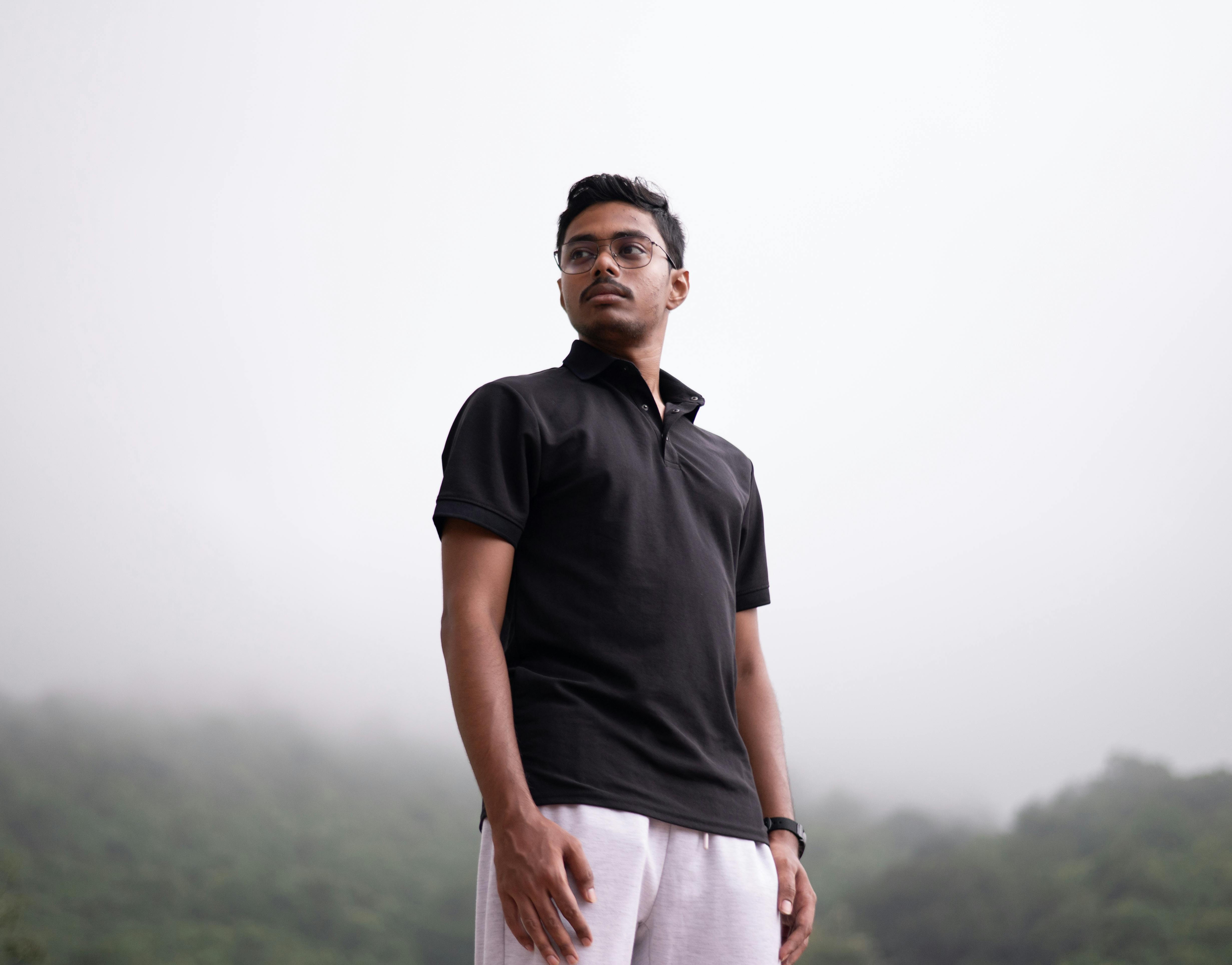 Portrait of a man in a black polo standing confidently against a misty outdoor landscape.
