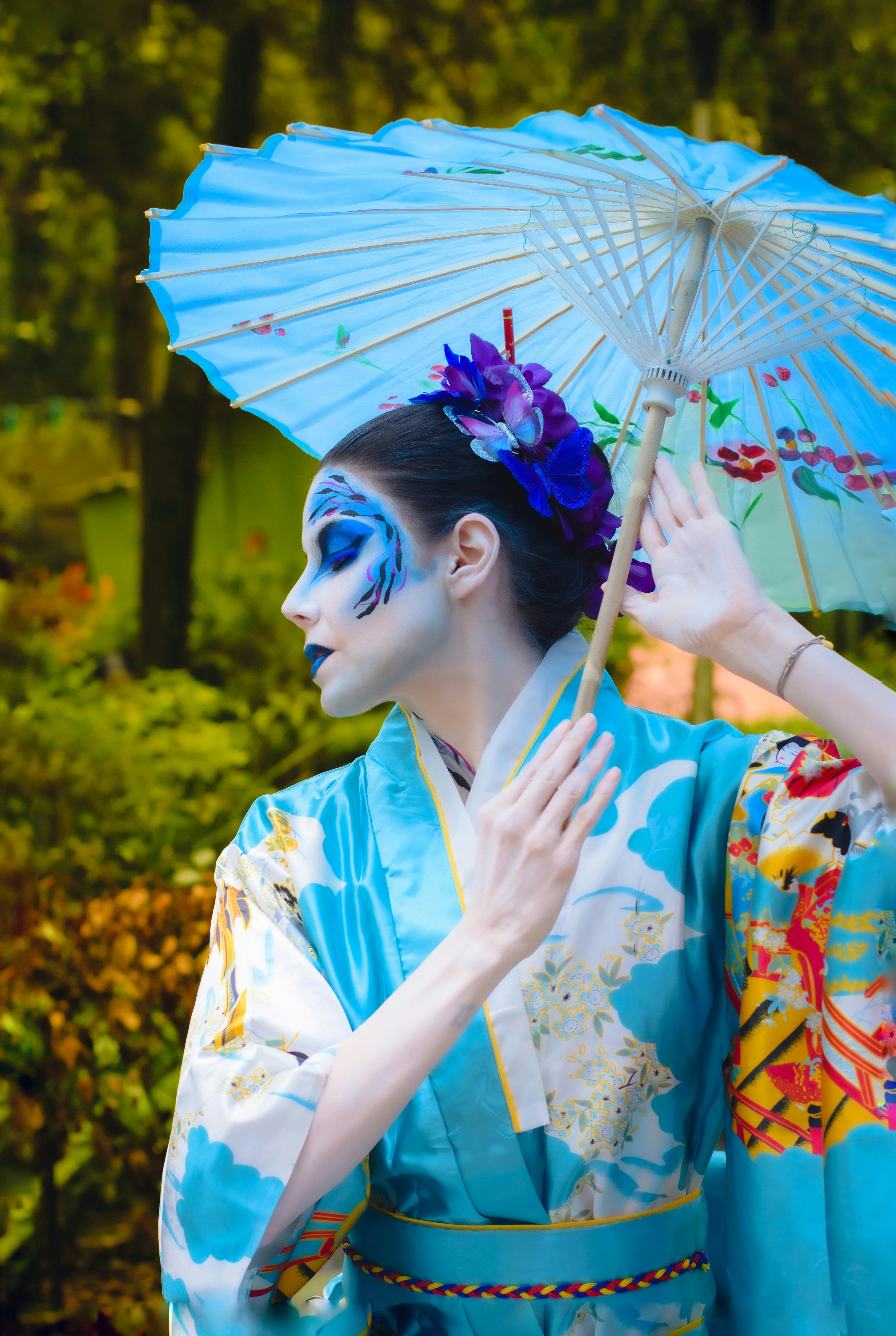 A woman in floral kimono with artistic makeup holds a parasol outdoors in summer.