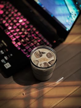 Chilled iced coffee on a desk with vibrant keyboard lighting, creating a warm and inviting workspace.