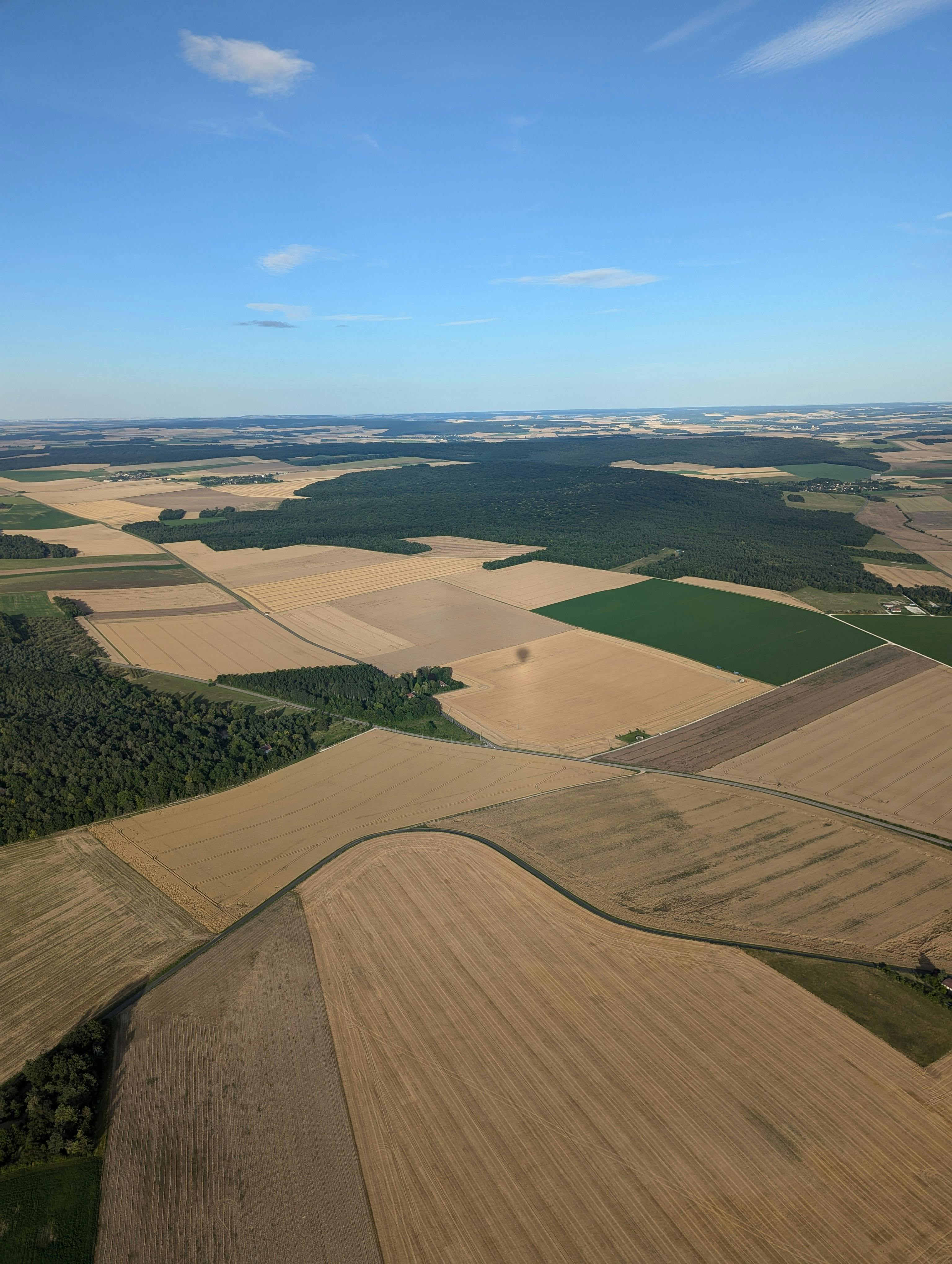 Expansive aerial view of varied agricultural fields and open countryside under a clear blue sky.