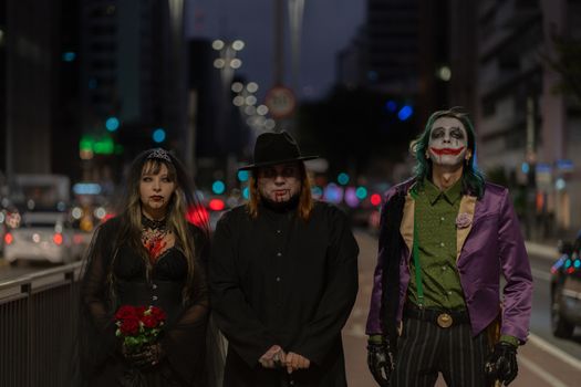 Three people in gothic Halloween costumes stand on a city street at night.