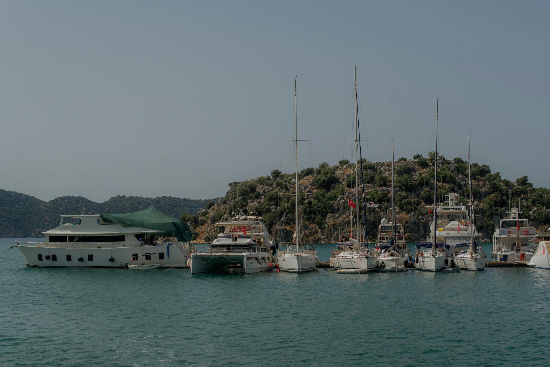 A beautiful collection of yachts docked at a harbor in Demre, Turkey against an island backdrop.