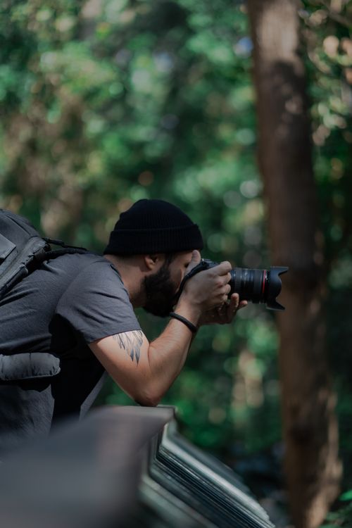 Free A photographer with a beanie takes a photo in a lush outdoor setting. Stock Photo