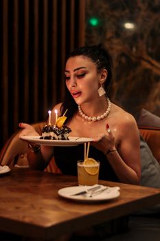 A stylish woman enjoying a birthday celebration in a cozy indoor setting, holding a cake with candles.