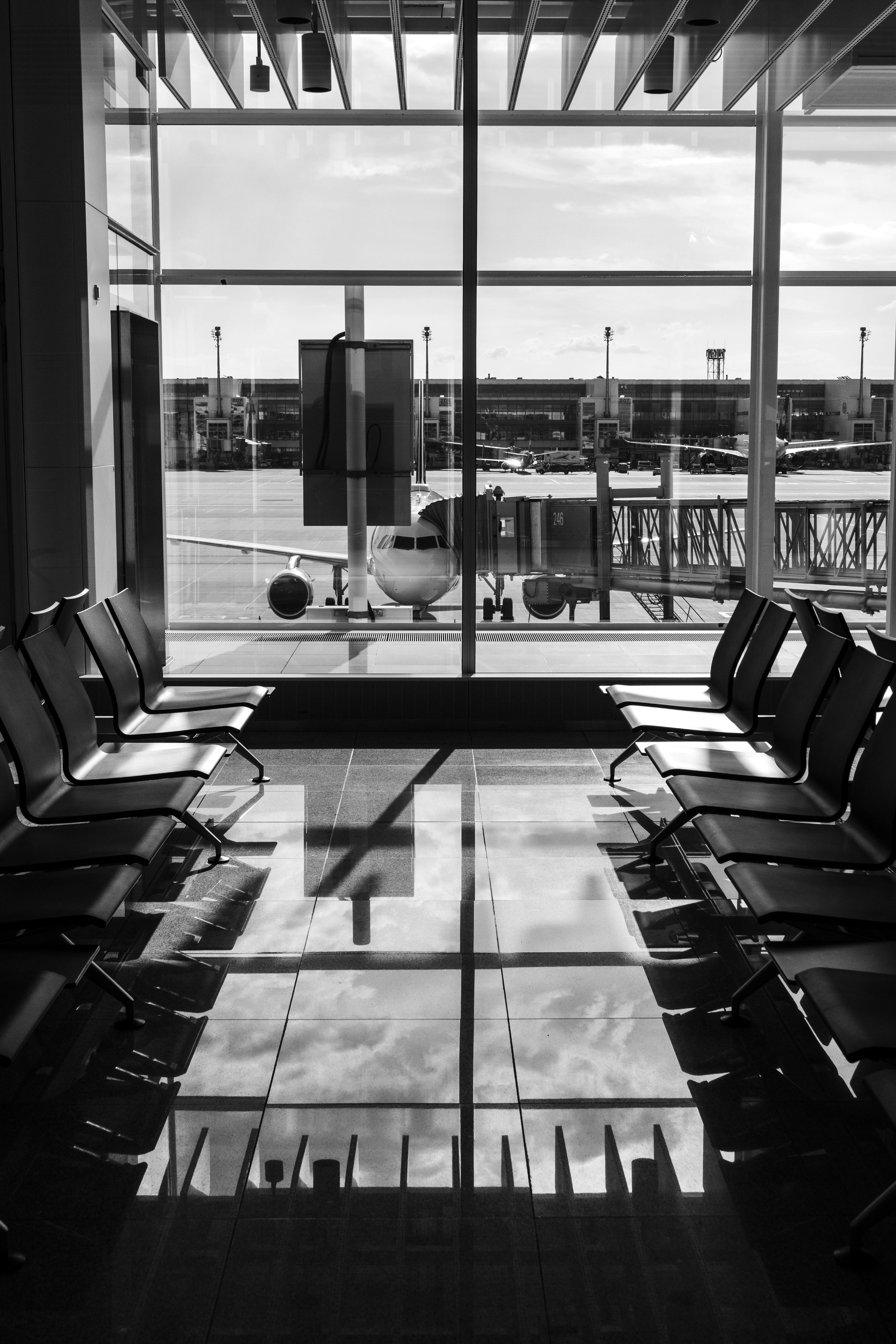 Black and white image of an empty airport terminal with a view of an airplane parked at the gate.