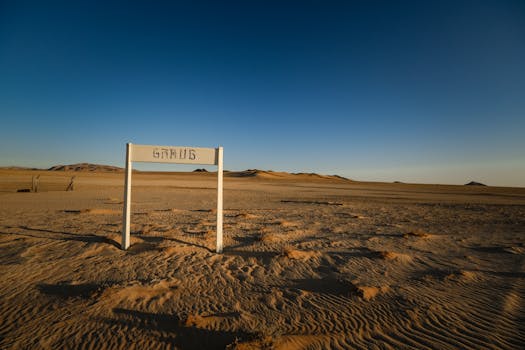 A vast, arid desert landscape with a solitary signpost under a clear sunset sky.