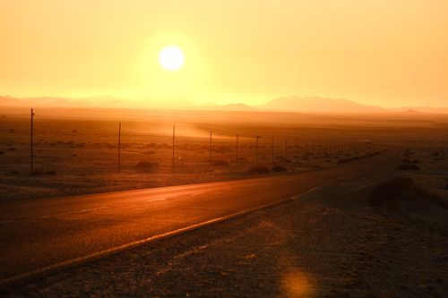Free A serene desert landscape with a road leading into a vibrant sunset, casting golden hues across the scene. Stock Photo