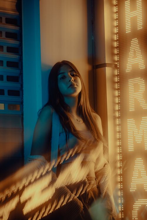 Free A young woman stands by a neon sign in the city, creating a moody urban vibe. Stock Photo