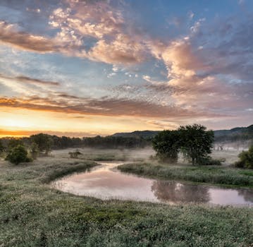 A tranquil sunrise landscape in Modena, WI, showcasing a reflective river and soft mist over a grassy field.