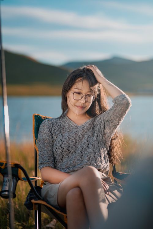 Free A serene portrait of a woman sitting by a lake, absorbing the summer sunset. Stock Photo