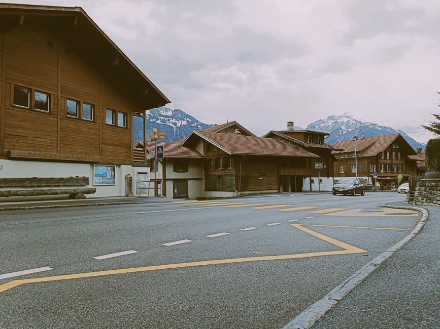 Scenic view of traditional Swiss chalets on a quiet street in Interlaken, Switzerland, near snow-capped mountains.