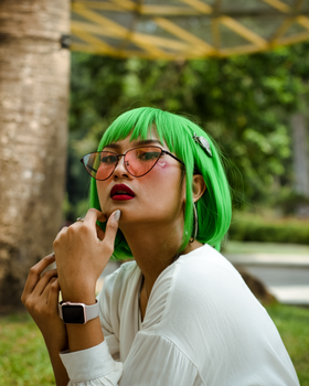 一位留着鲜艳绿发、戴着太阳镜的时尚女性，在宁静的户外环境中摆出姿势
