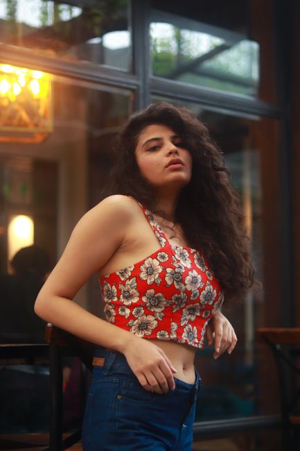 A woman with curly hair poses confidently in a floral crop top and jeans.