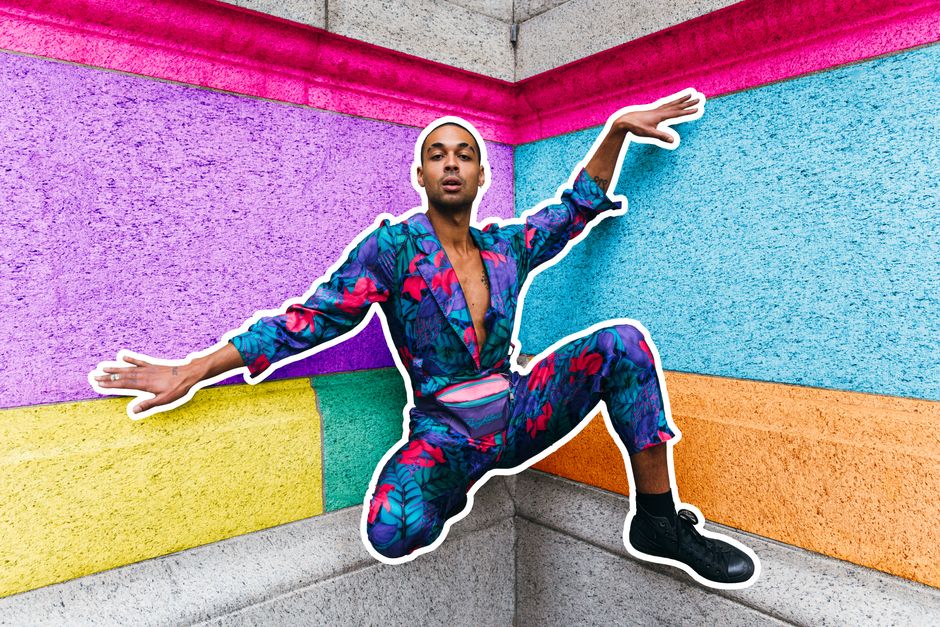 A stylish young man poses against a vibrant, multicolored wall, showcasing modern fashion and urban style.
