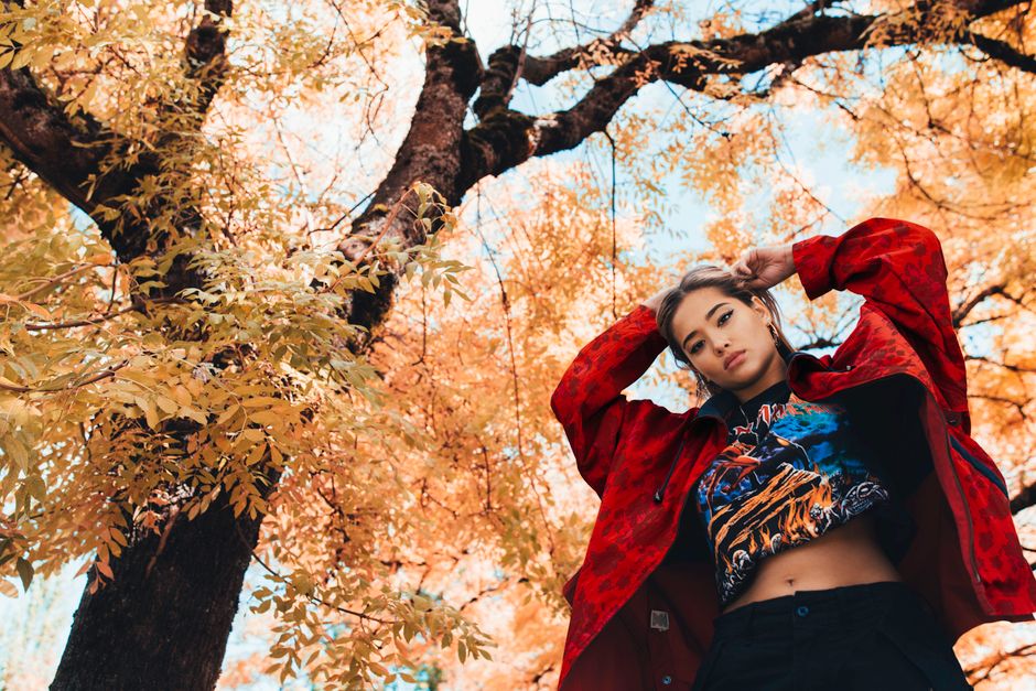 A stylish woman poses in a vibrant autumn setting. Editorial fashion under colorful trees.