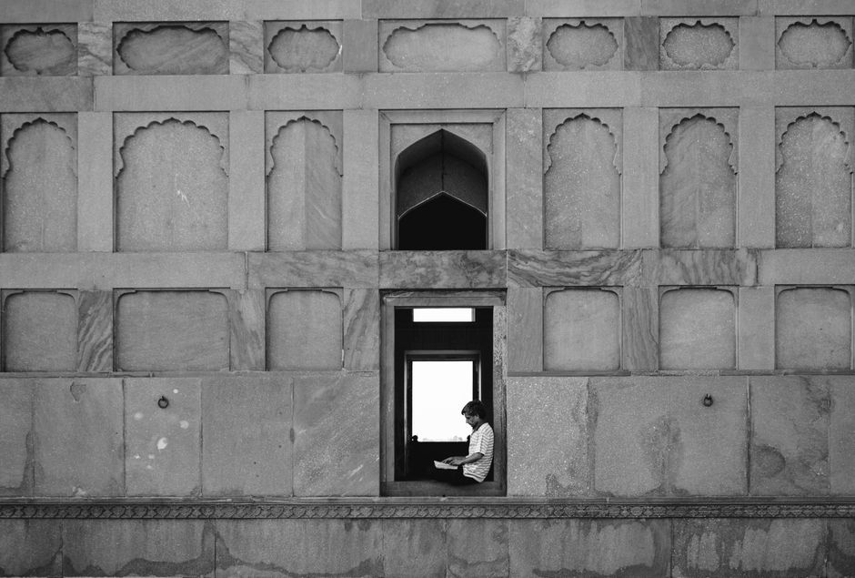 A man reading book by iconic Mughal architecture wall in Lahore, Pakistan.