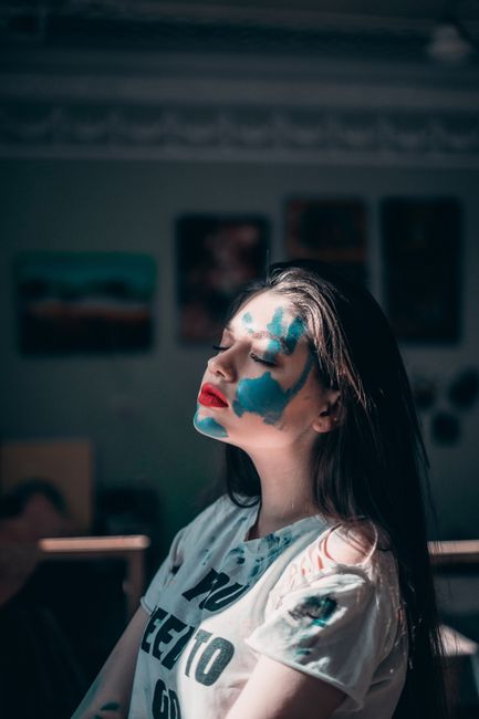 A creative portrait of a woman with vibrant blue face paint and red lips, embracing artistic expression.