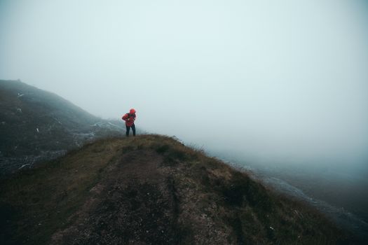 一位孤独的徒步旅行者身着红色夹克，穿越雾蒙蒙的山峰，拥抱大自然的孤寂