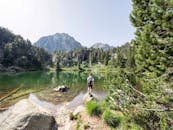 在西班牙的一个高山湖泊旁，一位徒步旅行者站在郁郁葱葱的绿植和风景秀丽的山丘之间