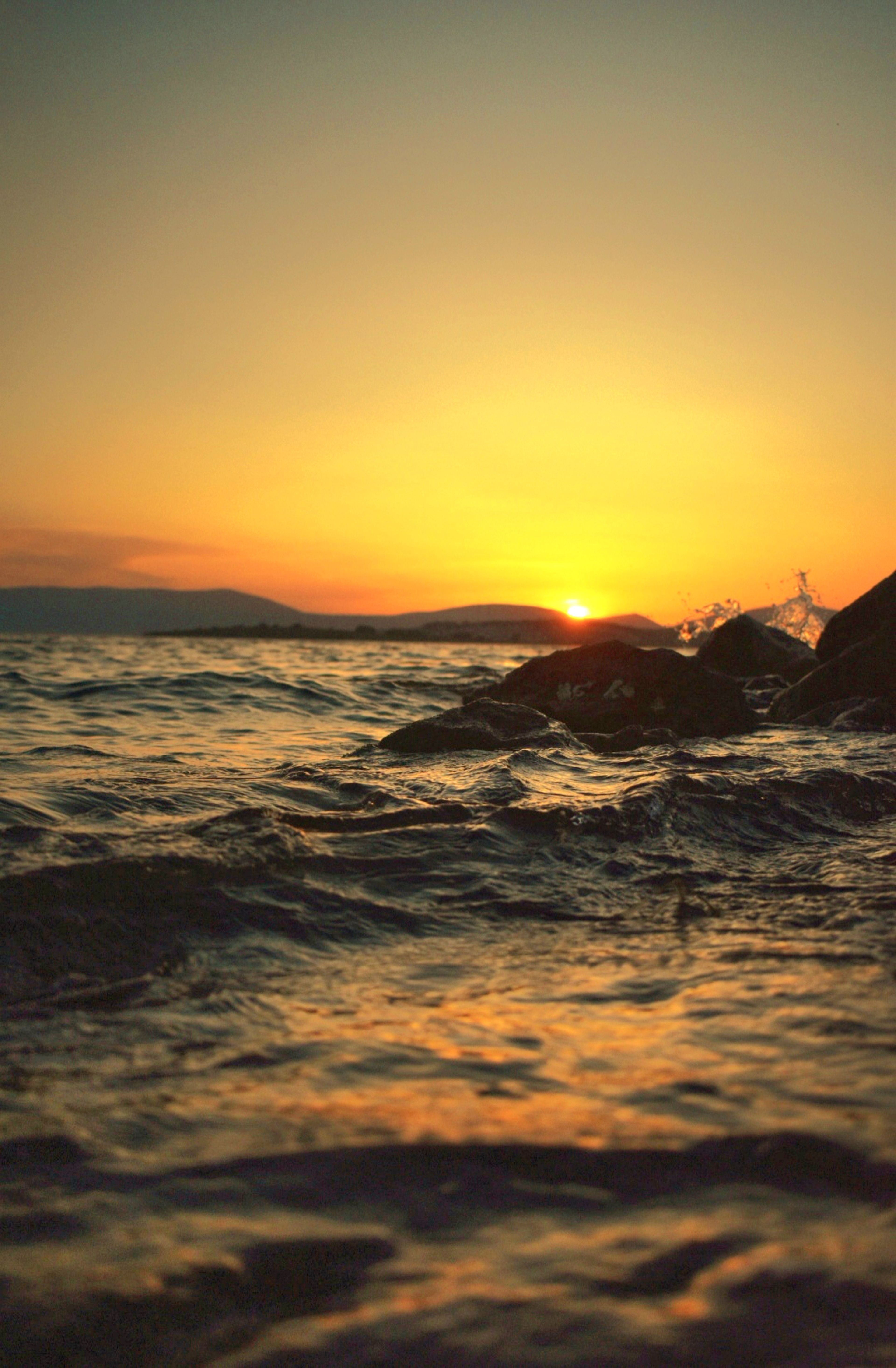 A sunset over the ocean with rocks and water · Free Stock Photo
