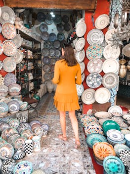 一名身穿橙色连衣裙的女子正在一家工匠店里浏览色彩鲜艳的陶瓷盘