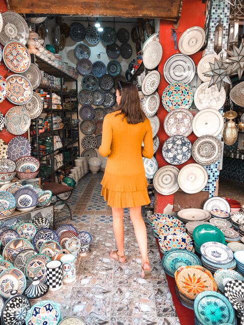 A woman in an orange dress browsing a vibrant display of ceramic plates in an artisan shop.