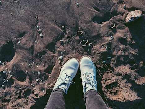 Perspective view of white boots standing on sandy beach with seashells at Shorncliffe, QLD.