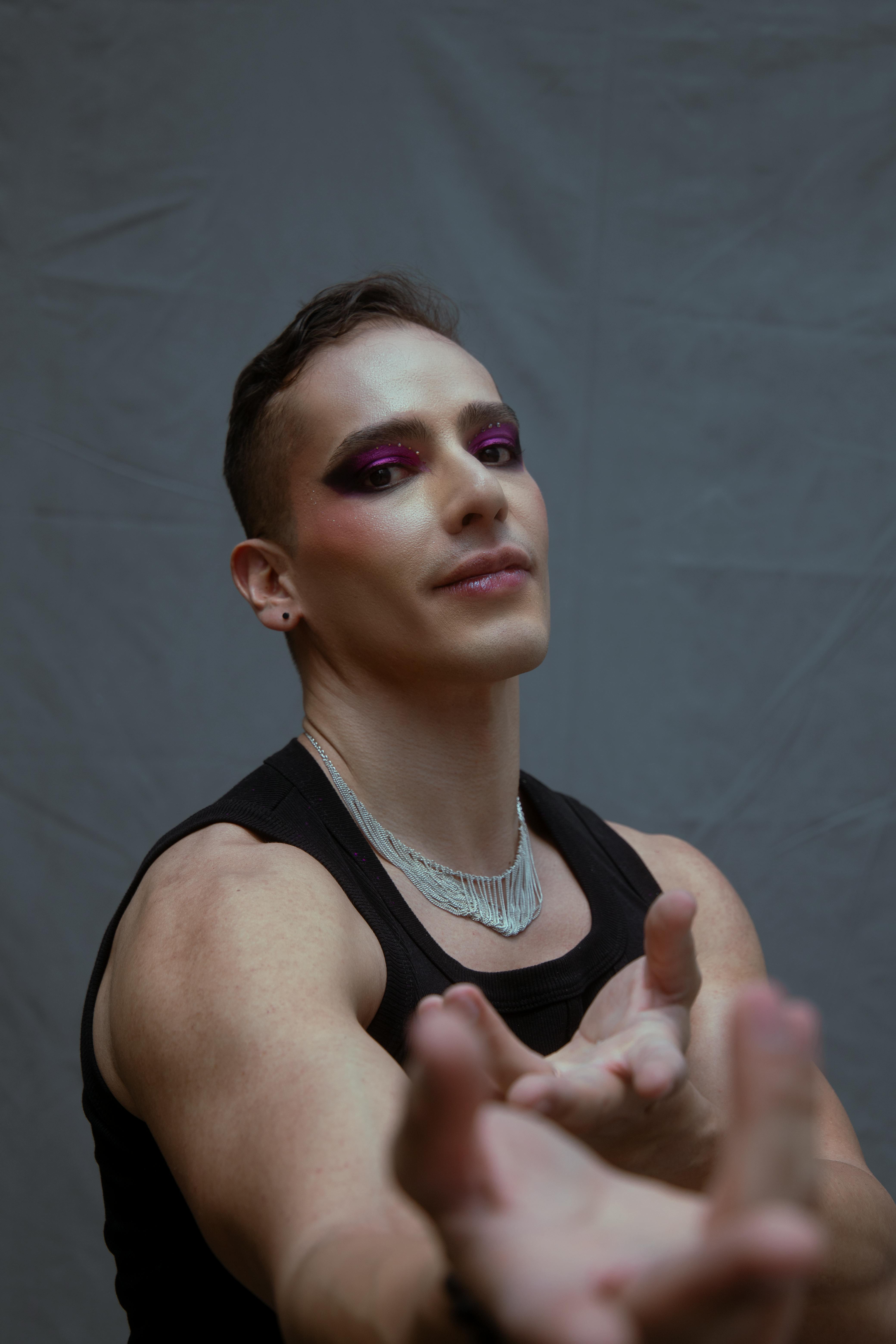 Free Vivid portrait of a young man wearing bold makeup and jewelry, posing confidently indoors. Stock Photo
