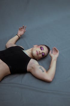 Stylish portrait of a woman wearing bold purple makeup, lying on a gray surface.