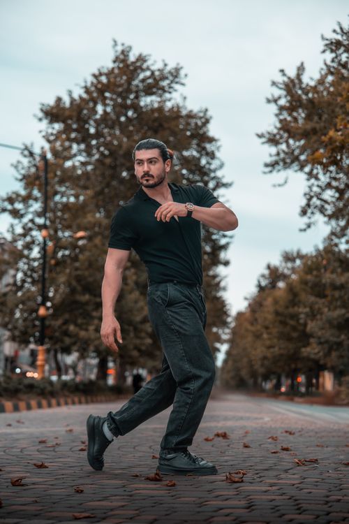 Free Man striking a dynamic pose on an urban street lined with autumn trees. Stock Photo