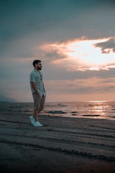 Man stands alone on the beach at sunset, gazing at the ocean waves.
