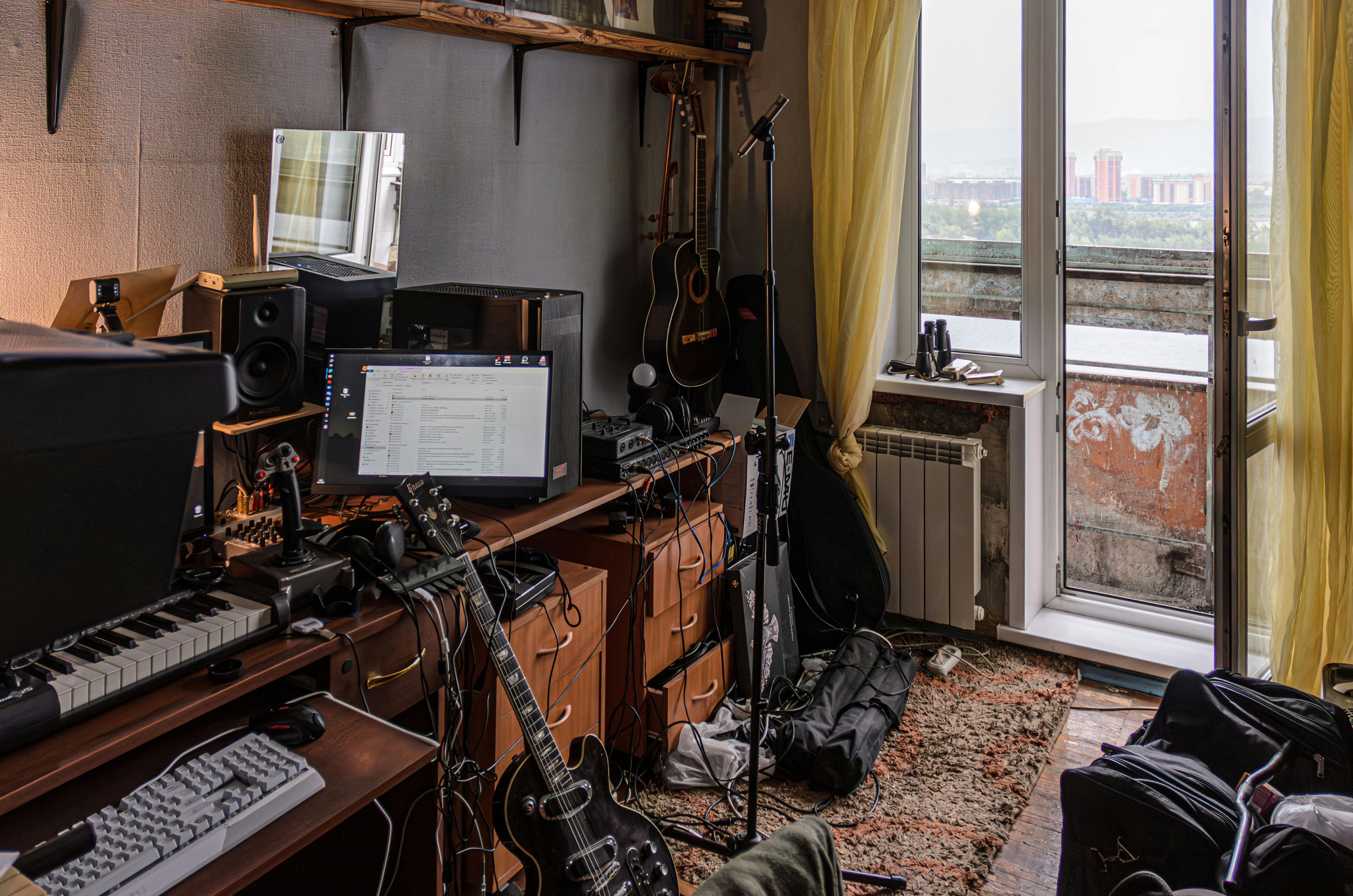 a room with a desk keyboard guitar and other musical equipment