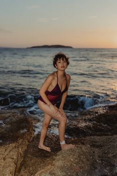 Woman in swimwear posing on a rocky beach during a beautiful sunset.