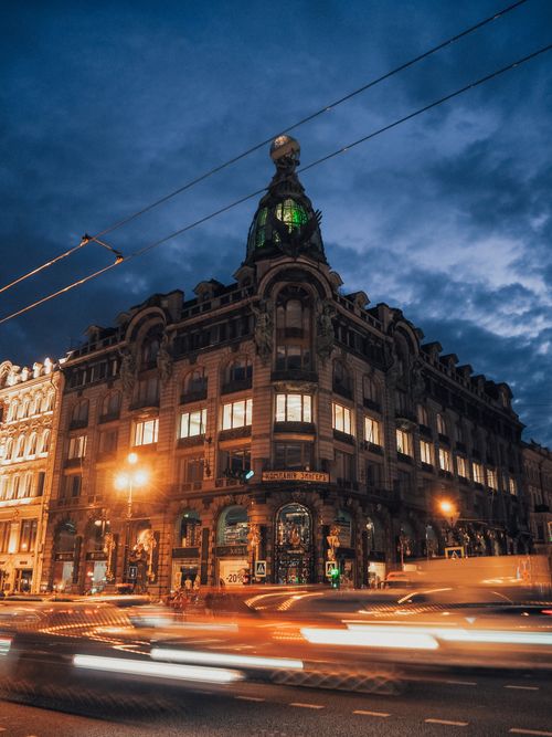 Free Night scene of Zinger House in Saint Petersburg with vibrant traffic under a dramatic sky. Stock Photo