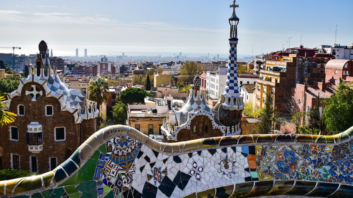 바르셀로나 — Gaudí's iconic mosaic architecture in Park Güell with a view of Barcelona's cityscape.