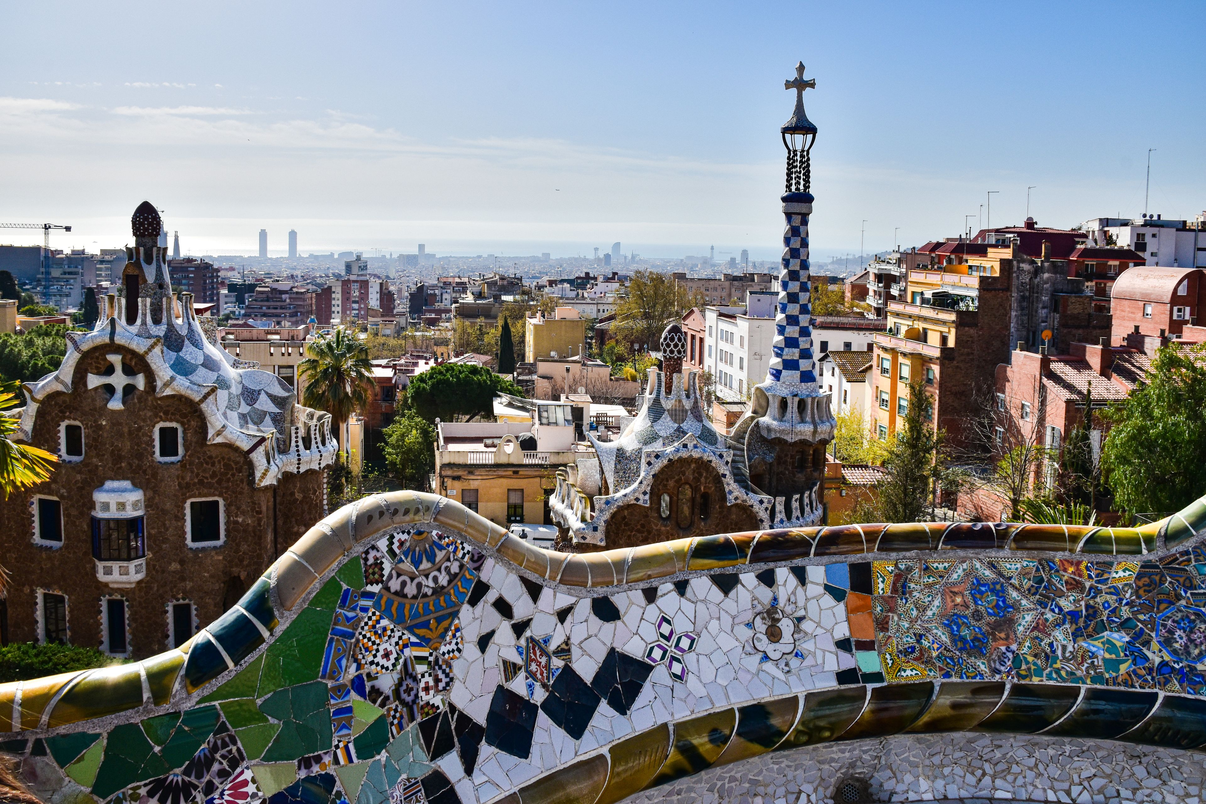 Gaudí's iconic mosaic architecture in Park Güell with a view of Barcelona's cityscape.