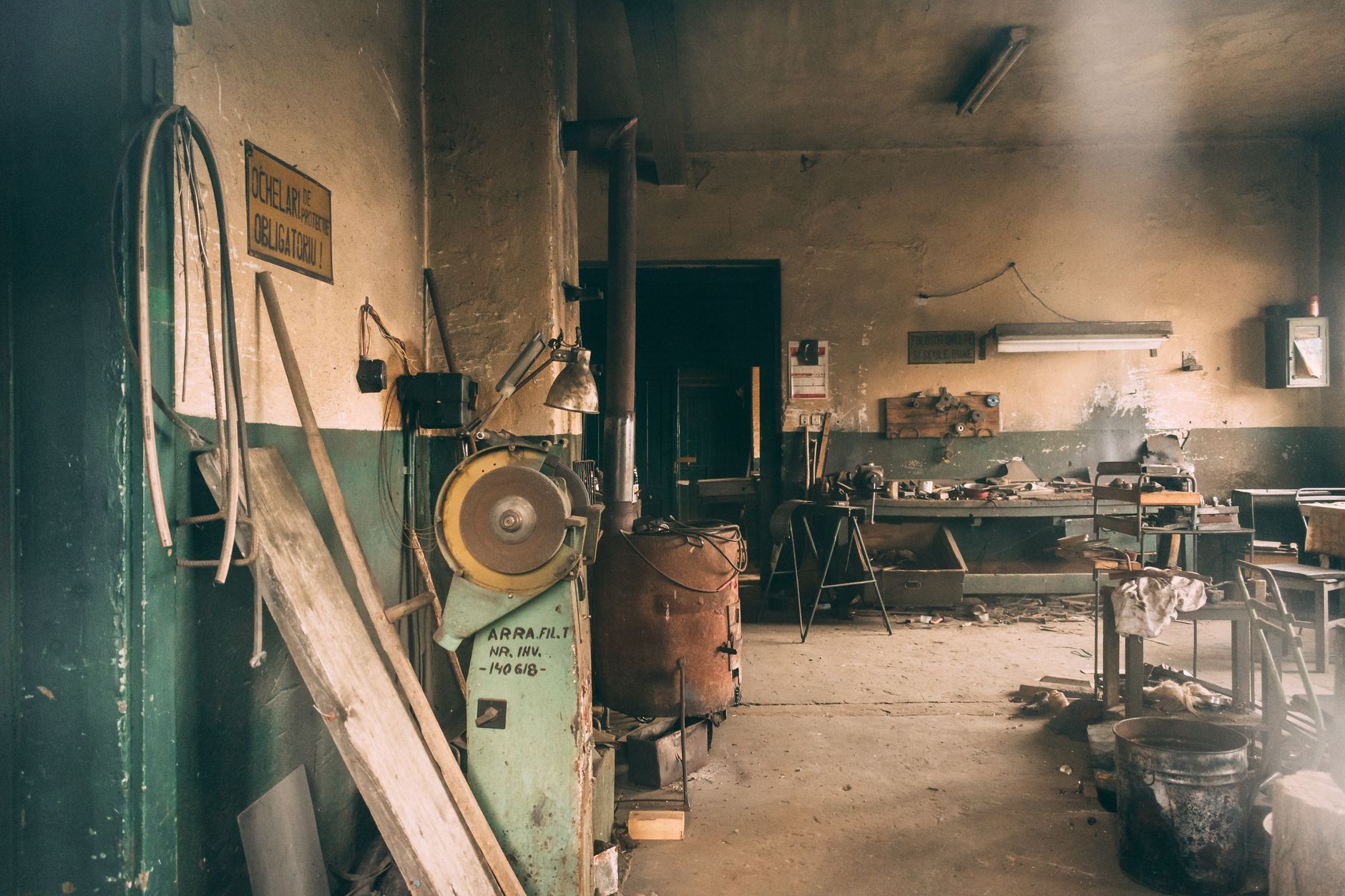Eski bir atölyenin loş ışığında, pencereden sızan tozlu gün ışığının aydınlattığı yıpranmış çalışma tezgahı ve geçmişin izlerini taşıyan nostaljik el aletleri.