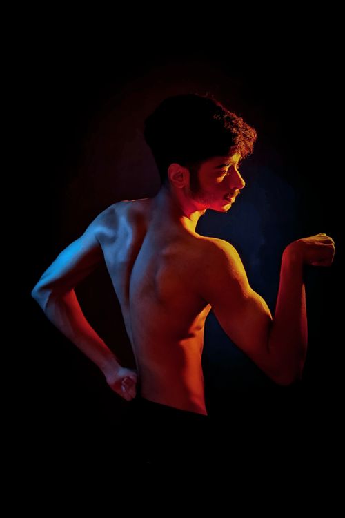 Free Creative portrait of a muscular man showcasing strength and physique in dramatic colored lighting. Stock Photo