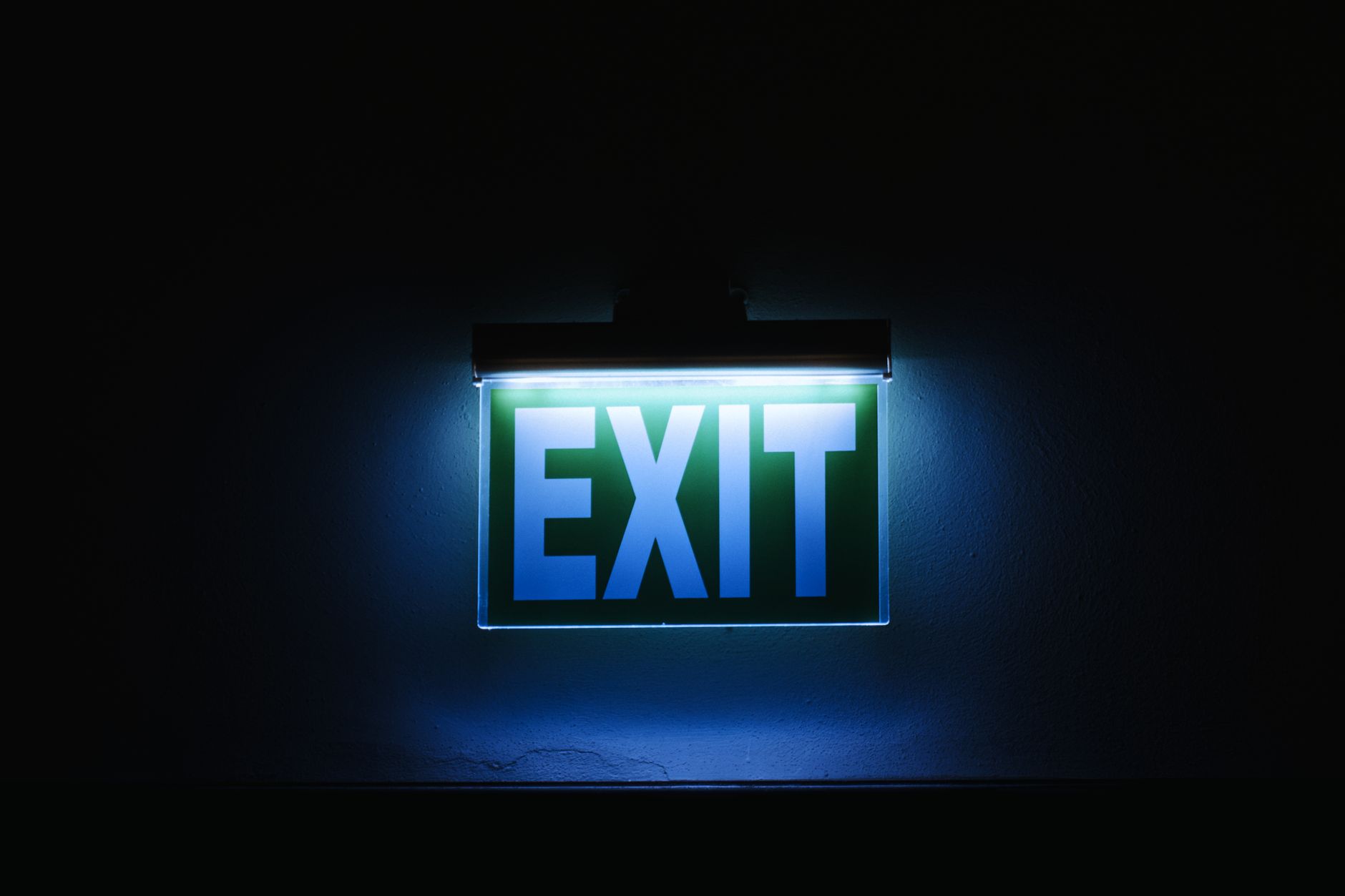 Photo of a glowing green exit sign in a dark environment, symbolizing safety and direction.
