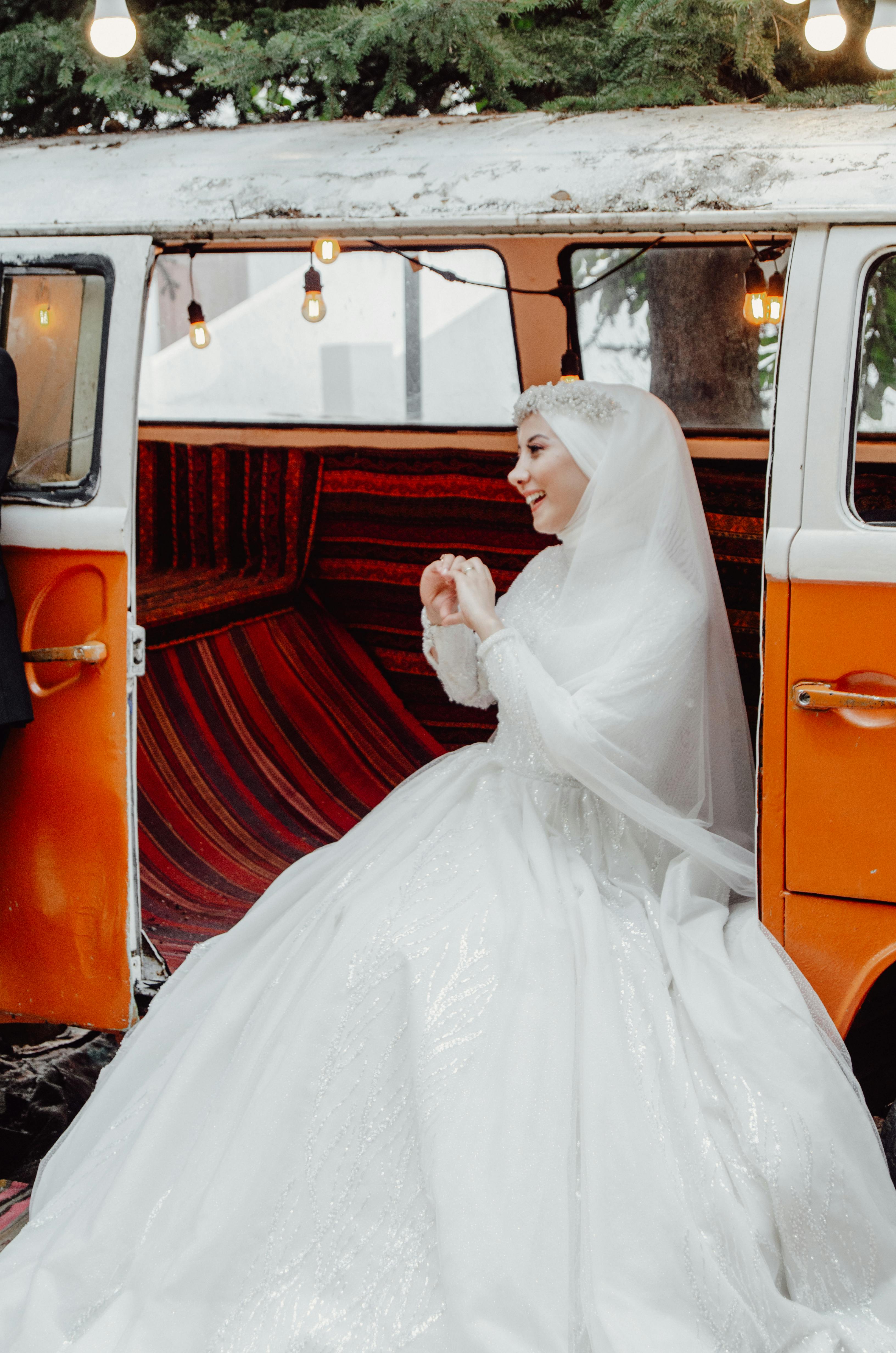 Mariée dans une robe blanche assise à côté d'un Combi VW décoré pour un mariage