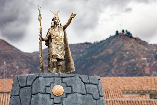 A majestic Inca statue stands prominently in Cusco, Peru with the Andes mountain range in the background.