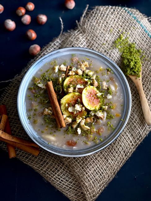 A bowl of traditional Turkish ashure topped with fresh figs, nuts, and cinnamon sticks.