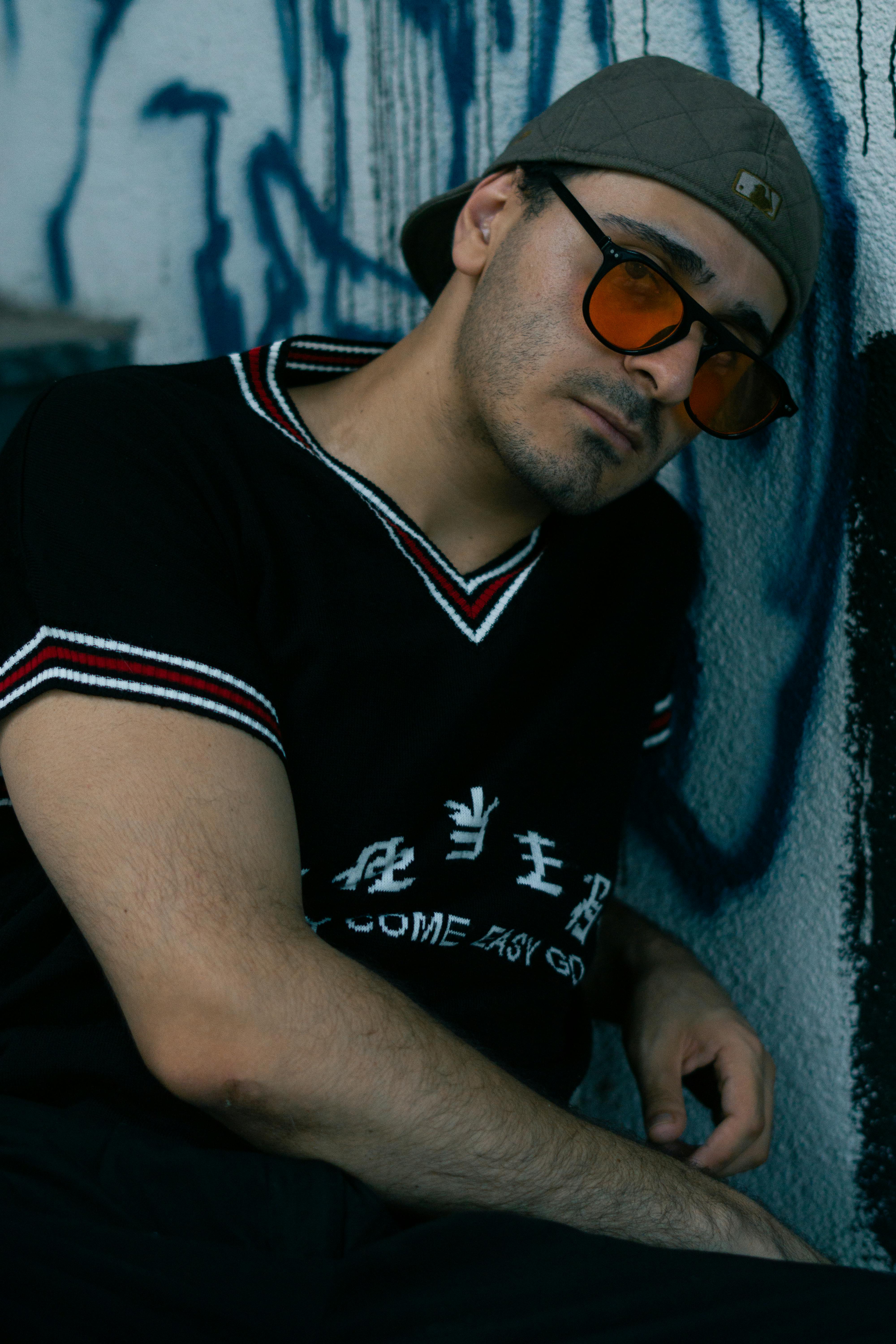 a man leaning against a wall with a baseball cap on