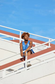 Stylish portrait of a woman sitting on a railing under a clear blue sky in Berlin, Germany.