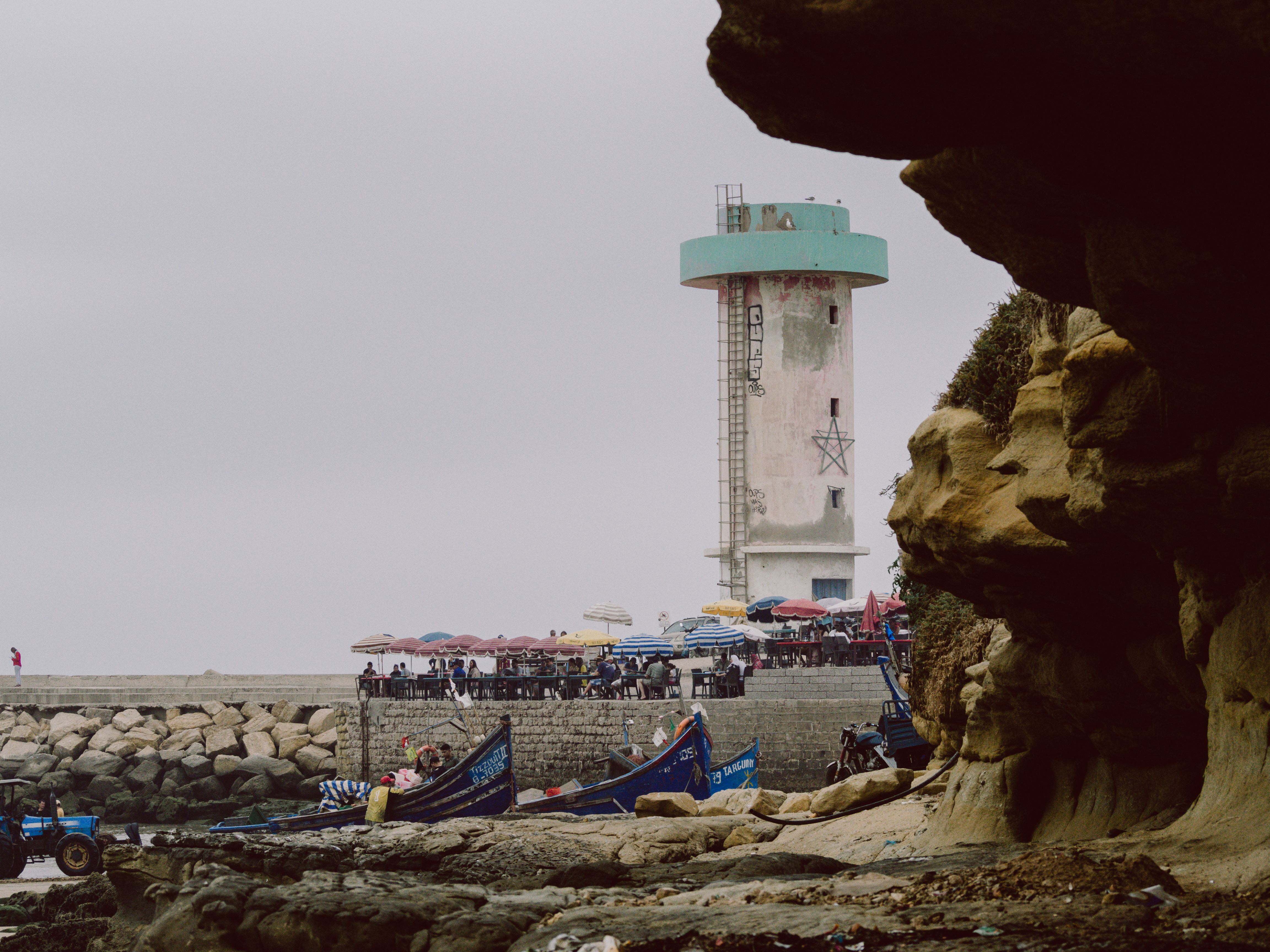 A scenic view of Imsouane's coastline featuring a lighthouse, fishing boats, and rocky cliffs.