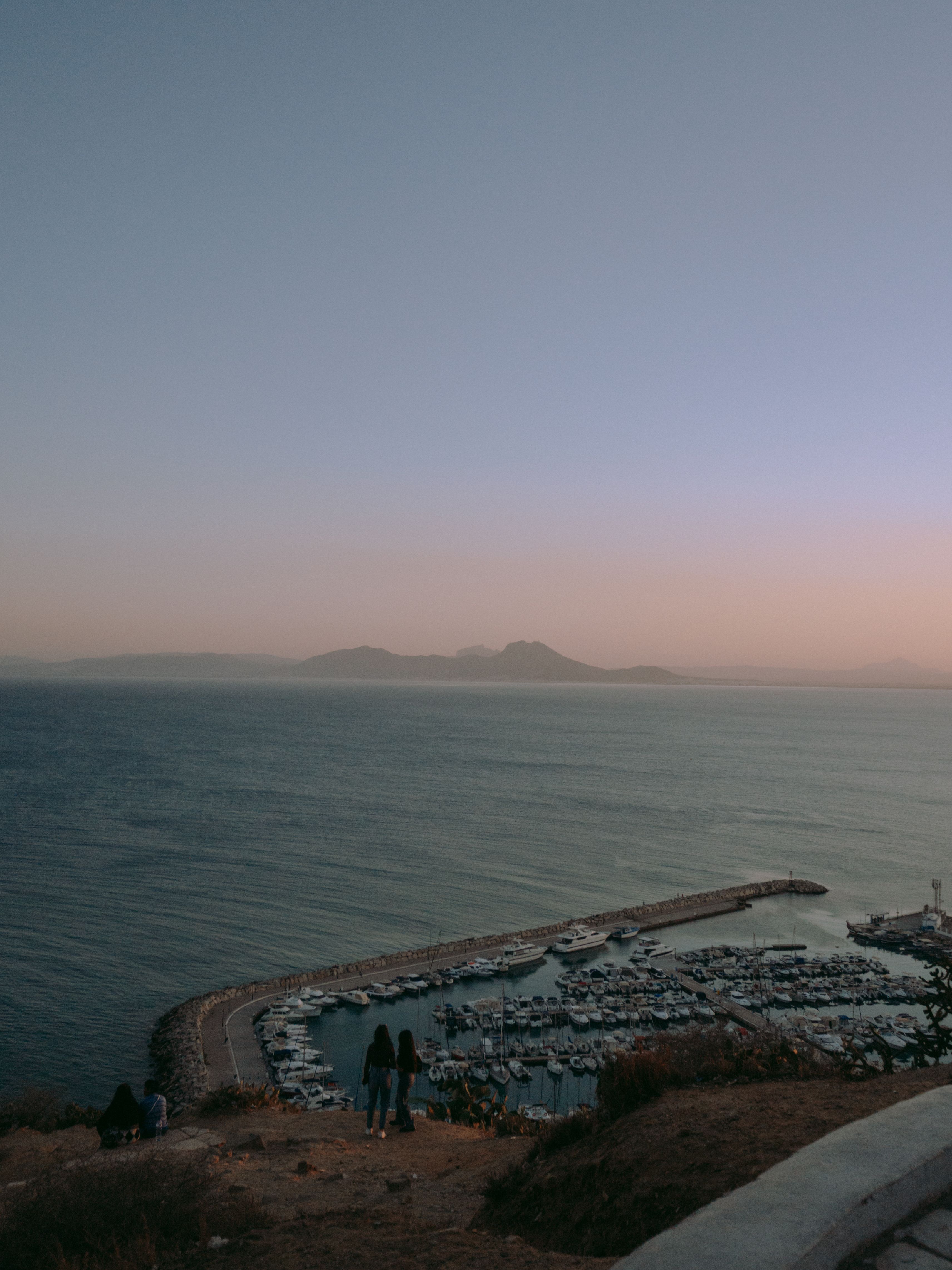 A serene view of a marina against a backdrop of mountains at dusk in Tunis, Tunisia.