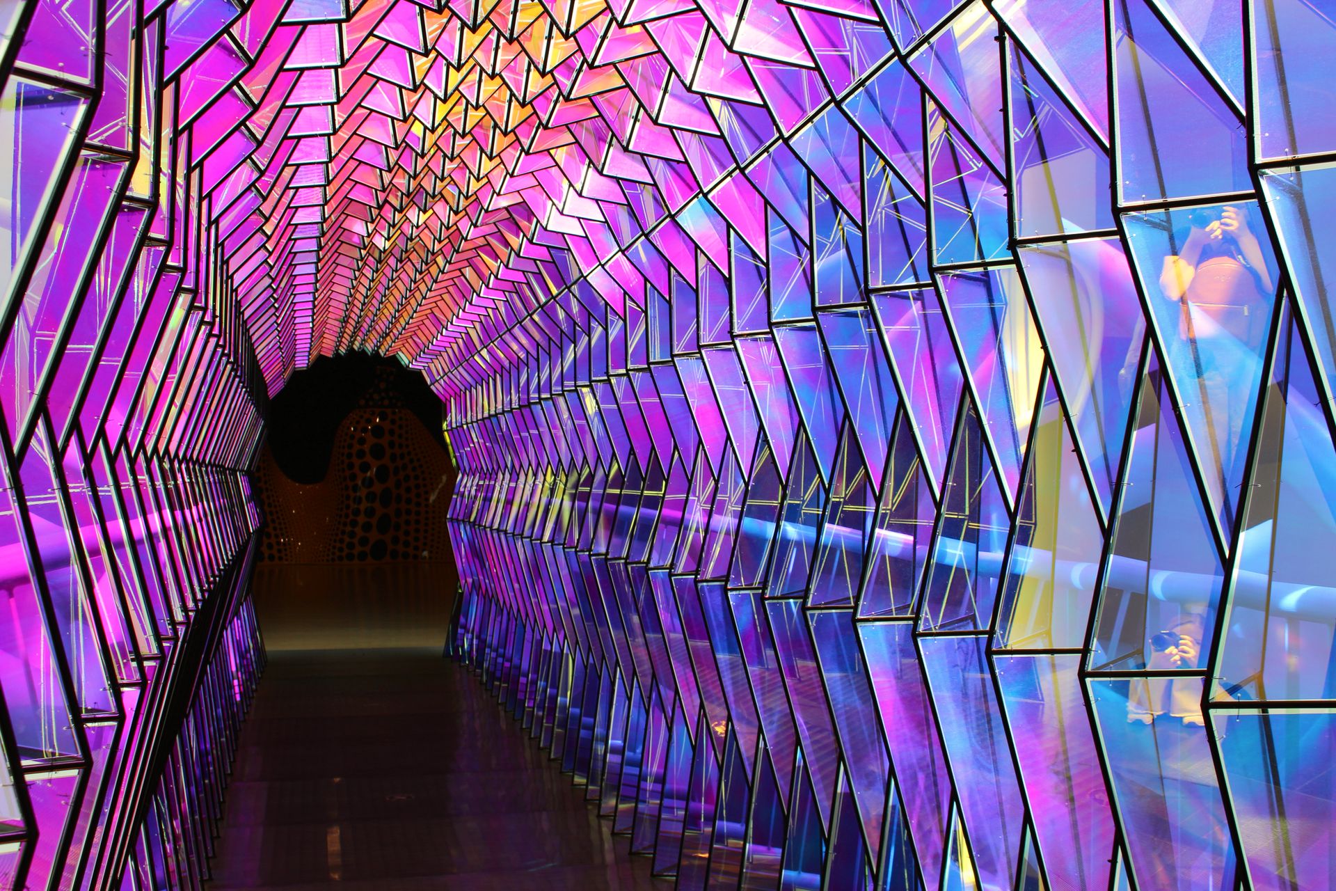 A colorful geometric tunnel featuring reflective and illuminated panels at a San Francisco exhibition.