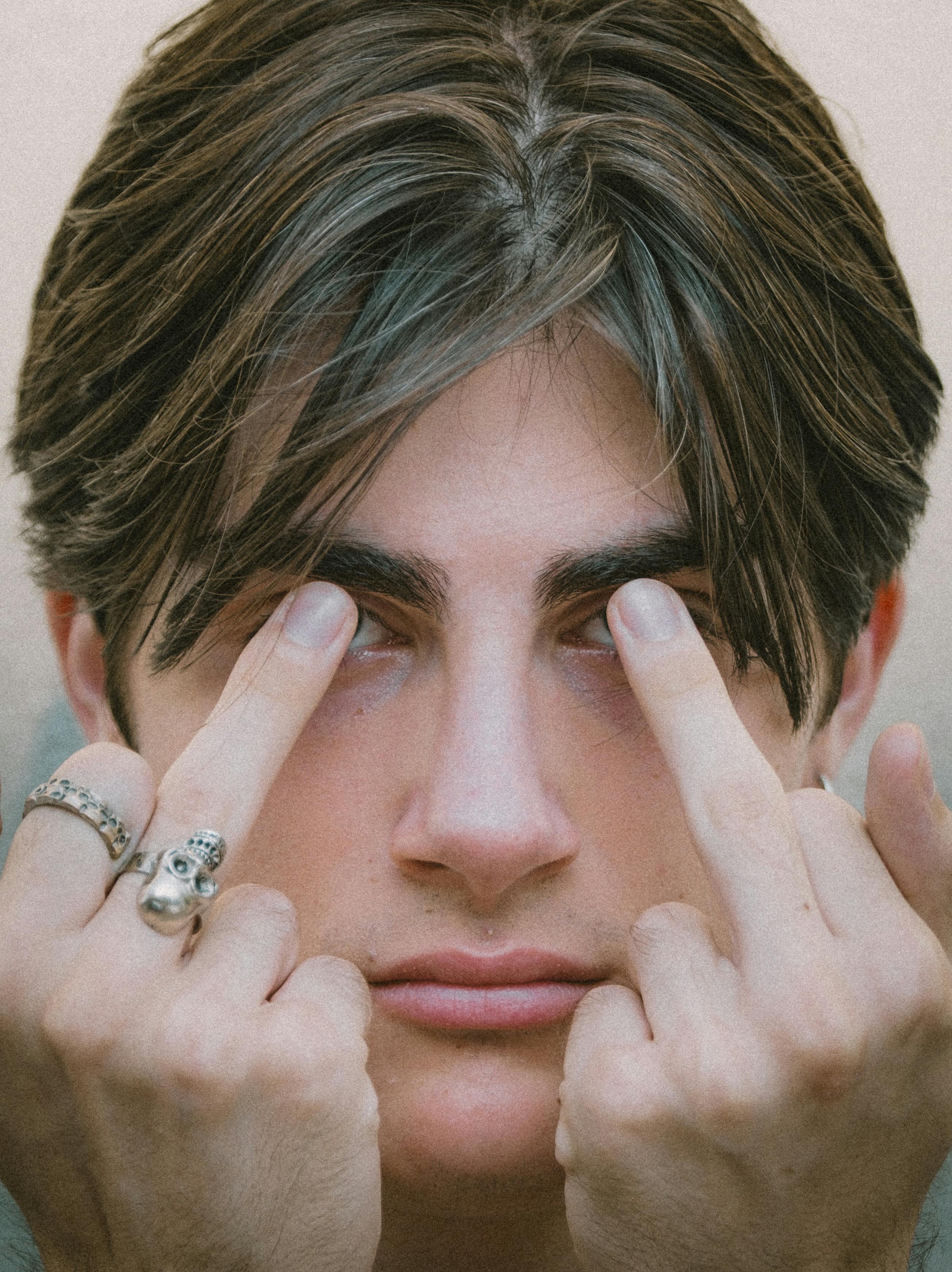 Close-up portrait of a young man with intense gaze and silver rings, conveying a bold expression.