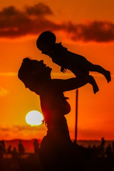 Silhouette of a mother lifting her child with a dramatic sunset backdrop in Cabedelo, Brazil.