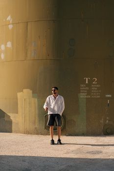 Man in white shirt and shorts against an industrial tank in İstanbul, Türkiye.